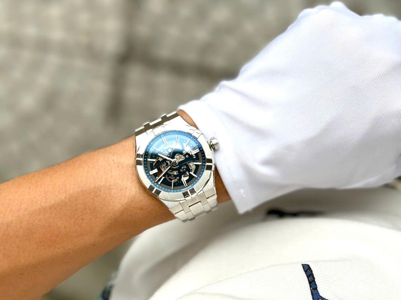 MAURICE LACROIX AIKON SKELETON AI6008-SS002-031-1 – NGHỆ THUẬT CƠ KHÍ PHÔ DIỄN TRỌN VẸN  Trong thế giới đồng hồ cơ hiện đại, skeleton watch luôn là sân chơi dành cho những người yêu thích kỹ thuật chế tác và vẻ đẹp cơ khí thuần túy.  Aikon Skeleton AI6008-SS002-031-1 chính là lời khẳng định mạnh mẽ của Maurice Lacroix trong phân khúc luxury sport watch với thiết kế lộ cơ toàn phần đầy cuốn hút.  👉 Skeleton hóa gần như toàn bộ mặt số  👉 Quan sát trực tiếp chuyển động bánh răng và cầu máy  👉 Integrated bracelet thể thao sang trọng  👉 Hoàn thiện cao cấp chuẩn Swiss Made  Đây là mẫu đồng hồ có khả năng tạo ấn tượng mạnh ngay từ lần đầu nhìn thấy.  THIẾT KẾ SKELETON TOÀN PHẦN – VẺ ĐẸP KHÔNG GÓC CHẾT  Điểm nổi bật nhất của AI6008-SS002-031-1 chính là kiến trúc skeleton xuyên thấu từ trước ra sau.  👉 Open-worked dial hoàn toàn  👉 Cầu máy được cắt gọt đối xứng  👉 Hiển thị toàn bộ hoạt động của bộ truyền động  👉 Tạo chiều sâu thị giác cực kỳ ấn tượng  Mỗi chuyển động của bánh răng, bánh lắc và hệ thống truyền động đều được phô diễn trực tiếp trước mắt người đeo.  Đây là kiểu đồng hồ mà người chơi có thể ngắm nhìn hàng giờ mà không cảm thấy nhàm chán.  DNA AIKON – MỘT TRONG NHỮNG THIẾT KẾ INTEGRATED BRACELET ĐƯỢC ƯA CHUỘNG NHẤT  Aikon được xem là bộ sưu tập thành công nhất của Maurice Lacroix trong nhiều năm gần đây.  Thiết kế nổi bật với:  👉 Bezel đặc trưng 6 càng đánh bóng  👉 Dây integrated bracelet liền khối  👉 Bề mặt hoàn thiện xen kẽ brushed và polished  👉 Cảm giác thể thao nhưng vẫn sang trọng  Nhờ ngôn ngữ thiết kế này, Aikon thường được giới chơi đồng hồ gọi là lựa chọn cực kỳ hấp dẫn trong phân khúc luxury sport watch Thụy Sĩ.  HOÀN THIỆN VỎ THÉP CAO CẤP  Maurice Lacroix luôn nổi tiếng về chất lượng hoàn thiện vượt tầm giá.  Trên AI6008-SS002-031-1, người dùng dễ dàng nhận thấy:  👉 Các bề mặt chải xước satin sắc nét  👉 Cạnh vát đánh bóng tinh tế  👉 Sự chuyển tiếp giữa các lớp hoàn thiện cực kỳ mượt mà  👉 Tạo hiệu ứng ánh sáng đẹp ở mọi góc nhìn  Những chi tiết này giúp chiếc đồng hồ mang cảm giác cao cấp hơn đáng kể so với nhiều mẫu skeleton cùng phân khúc.  SIZE 42MM – ĐẬM CHẤT SPORT WATCH HIỆN ĐẠI  👉 Đường kính 42mm  👉 Độ dày 11mm  Tỷ lệ này giúp chiếc đồng hồ đạt được sự cân bằng giữa:  Tính thể thao Độ hiện diện trên cổ tay Sự thoải mái khi sử dụng hàng ngày  Kết hợp cùng thiết kế càng nối dây ngắn và ôm tay, AIKON Skeleton phù hợp với phần lớn cổ tay nam từ khoảng 16.5cm trở lên.  BỘ MÁY ML135 – TRÁI TIM CỦA TÁC PHẨM SKELETON  Ẩn sau kiến trúc lộ cơ là bộ máy Maurice Lacroix Calibre ML135.  Thông số nổi bật:  👉 Automatic movement  👉 26 chân kính  👉 Tần số dao động 28.800 vph  👉 Trữ cót khoảng 38 giờ  👉 Hiển thị giờ, phút và giây  Bộ máy được skeleton hóa nhằm phô diễn tối đa các thành phần cơ khí bên trong, đồng thời vẫn duy trì độ ổn định và độ bền cao trong quá trình sử dụng hàng ngày.  KÍNH SAPPHIRE PHỦ AR – TỐI ƯU TRẢI NGHIỆM QUAN SÁT  Để khai thác tối đa vẻ đẹp của bộ máy skeleton, Maurice Lacroix trang bị:  👉 Kính sapphire chống xước  👉 Lớp phủ chống phản chiếu AR (Anti-Reflective)  👉 Caseback sapphire trong suốt  Nhờ đó người đeo có thể quan sát rõ từng chi tiết cơ khí kể cả dưới điều kiện ánh sáng mạnh.  CHỐNG NƯỚC 200M – HIẾM GẶP TRONG THẾ GIỚI SKELETON  Một trong những ưu điểm đáng giá nhất của AIKON Skeleton chính là khả năng chống nước lên tới 20ATM (200m).  👉 Đi bơi thoải mái  👉 Sử dụng hàng ngày an tâm  👉 Độ kín nước vượt trội trong phân khúc skeleton watch  Đây là thông số hiếm thấy trên các mẫu đồng hồ lộ cơ vốn thường tập trung vào tính trình diễn hơn là khả năng vận hành thực tế.  TRẢI NGHIỆM ĐEO THỰC TẾ  AIKON Skeleton mang lại cảm giác rất khác biệt so với những mẫu đồng hồ truyền thống.  👉 Hiện đại  👉 Cá tính  👉 Đậm chất cơ khí  👉 Sang trọng theo phong cách contemporary luxury  Đây là mẫu đồng hồ dành cho người thích thể hiện gu chơi đồng hồ và muốn sở hữu một thiết kế nổi bật giữa đám đông.  GIÁ TRỊ SƯU TẦM & THANH KHOẢN  Maurice Lacroix Skeleton luôn có lượng sản phẩm xuất hiện trên thị trường không nhiều.  Điểm hấp dẫn của AI6008-SS002-031-1 nằm ở:  👉 Thiết kế skeleton toàn phần cực kỳ bắt mắt  👉 Integrated bracelet đang là xu hướng của giới sưu tầm  👉 Hoàn thiện cao cấp chuẩn Swiss Made  👉 Khả năng chống nước 200m hiếm gặp  👉 Giá trị trải nghiệm vượt xa mức đầu tư  Đây là mẫu đồng hồ rất đáng cân nhắc cho những ai muốn bước vào thế giới skeleton luxury watch với một thiết kế khác biệt và giàu tính kỹ thuật.  MAURICE LACROIX AIKON SKELETON PHÙ HỢP VỚI AI?  👉 Người yêu thích đồng hồ skeleton và nghệ thuật cơ khí  👉 Người muốn một luxury sport watch khác biệt với số đông  👉 Người thích thiết kế integrated bracelet hiện đại  👉 Nhà sưu tầm tìm kiếm những mẫu Swiss Made ít gặp  👉 Người cần một chiếc đồng hồ vừa nổi bật vừa có tính ứng dụng cao hàng ngày  MUA ĐỒNG HỒ LƯỚT Ở ĐÂU UY TÍN?  Nếu bạn đang tìm một địa chỉ mua bán đồng hồ đã qua sử dụng chính hãng tại TP.HCM, SGWatch là lựa chọn cân nhắc.  👉 Cam kết chính hãng 100%  👉 Hỗ trợ thu đổi – lên đời  👉 Hỗ trợ hoạt động hỗ trợ  👉 Giao hàng tốc độ miễn phí  📍 1415 Phan Văn Trị, Phường 10, Gò Vấp  📞 0942.951.951 – 093.3035.666