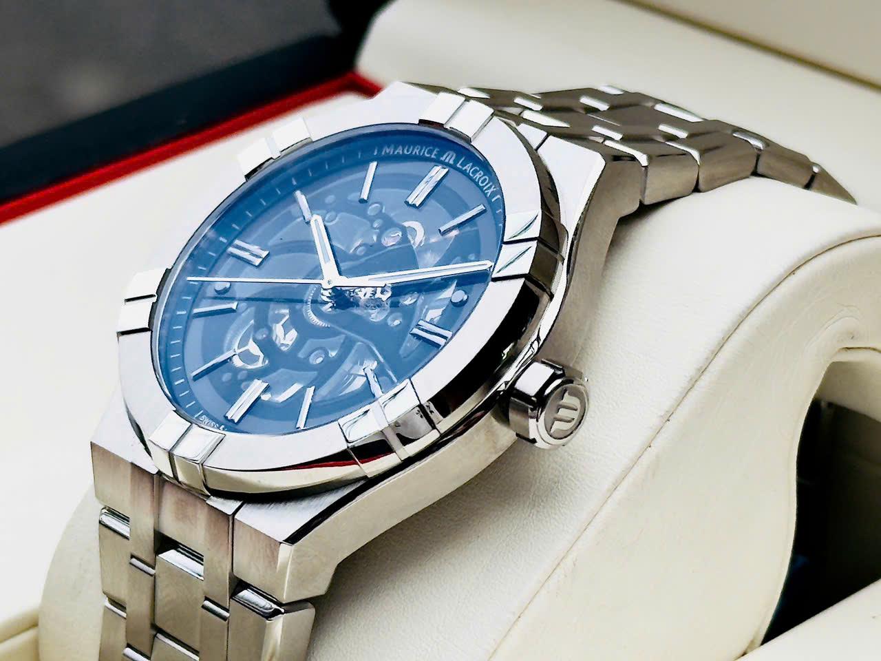 MAURICE LACROIX AIKON SKELETON AI6008-SS002-031-1 – NGHỆ THUẬT CƠ KHÍ PHÔ DIỄN TRỌN VẸN  Trong thế giới đồng hồ cơ hiện đại, skeleton watch luôn là sân chơi dành cho những người yêu thích kỹ thuật chế tác và vẻ đẹp cơ khí thuần túy.  Aikon Skeleton AI6008-SS002-031-1 chính là lời khẳng định mạnh mẽ của Maurice Lacroix trong phân khúc luxury sport watch với thiết kế lộ cơ toàn phần đầy cuốn hút.  👉 Skeleton hóa gần như toàn bộ mặt số  👉 Quan sát trực tiếp chuyển động bánh răng và cầu máy  👉 Integrated bracelet thể thao sang trọng  👉 Hoàn thiện cao cấp chuẩn Swiss Made  Đây là mẫu đồng hồ có khả năng tạo ấn tượng mạnh ngay từ lần đầu nhìn thấy.  THIẾT KẾ SKELETON TOÀN PHẦN – VẺ ĐẸP KHÔNG GÓC CHẾT  Điểm nổi bật nhất của AI6008-SS002-031-1 chính là kiến trúc skeleton xuyên thấu từ trước ra sau.  👉 Open-worked dial hoàn toàn  👉 Cầu máy được cắt gọt đối xứng  👉 Hiển thị toàn bộ hoạt động của bộ truyền động  👉 Tạo chiều sâu thị giác cực kỳ ấn tượng  Mỗi chuyển động của bánh răng, bánh lắc và hệ thống truyền động đều được phô diễn trực tiếp trước mắt người đeo.  Đây là kiểu đồng hồ mà người chơi có thể ngắm nhìn hàng giờ mà không cảm thấy nhàm chán.  DNA AIKON – MỘT TRONG NHỮNG THIẾT KẾ INTEGRATED BRACELET ĐƯỢC ƯA CHUỘNG NHẤT  Aikon được xem là bộ sưu tập thành công nhất của Maurice Lacroix trong nhiều năm gần đây.  Thiết kế nổi bật với:  👉 Bezel đặc trưng 6 càng đánh bóng  👉 Dây integrated bracelet liền khối  👉 Bề mặt hoàn thiện xen kẽ brushed và polished  👉 Cảm giác thể thao nhưng vẫn sang trọng  Nhờ ngôn ngữ thiết kế này, Aikon thường được giới chơi đồng hồ gọi là lựa chọn cực kỳ hấp dẫn trong phân khúc luxury sport watch Thụy Sĩ.  HOÀN THIỆN VỎ THÉP CAO CẤP  Maurice Lacroix luôn nổi tiếng về chất lượng hoàn thiện vượt tầm giá.  Trên AI6008-SS002-031-1, người dùng dễ dàng nhận thấy:  👉 Các bề mặt chải xước satin sắc nét  👉 Cạnh vát đánh bóng tinh tế  👉 Sự chuyển tiếp giữa các lớp hoàn thiện cực kỳ mượt mà  👉 Tạo hiệu ứng ánh sáng đẹp ở mọi góc nhìn  Những chi tiết này giúp chiếc đồng hồ mang cảm giác cao cấp hơn đáng kể so với nhiều mẫu skeleton cùng phân khúc.  SIZE 42MM – ĐẬM CHẤT SPORT WATCH HIỆN ĐẠI  👉 Đường kính 42mm  👉 Độ dày 11mm  Tỷ lệ này giúp chiếc đồng hồ đạt được sự cân bằng giữa:  Tính thể thao Độ hiện diện trên cổ tay Sự thoải mái khi sử dụng hàng ngày  Kết hợp cùng thiết kế càng nối dây ngắn và ôm tay, AIKON Skeleton phù hợp với phần lớn cổ tay nam từ khoảng 16.5cm trở lên.  BỘ MÁY ML135 – TRÁI TIM CỦA TÁC PHẨM SKELETON  Ẩn sau kiến trúc lộ cơ là bộ máy Maurice Lacroix Calibre ML135.  Thông số nổi bật:  👉 Automatic movement  👉 26 chân kính  👉 Tần số dao động 28.800 vph  👉 Trữ cót khoảng 38 giờ  👉 Hiển thị giờ, phút và giây  Bộ máy được skeleton hóa nhằm phô diễn tối đa các thành phần cơ khí bên trong, đồng thời vẫn duy trì độ ổn định và độ bền cao trong quá trình sử dụng hàng ngày.  KÍNH SAPPHIRE PHỦ AR – TỐI ƯU TRẢI NGHIỆM QUAN SÁT  Để khai thác tối đa vẻ đẹp của bộ máy skeleton, Maurice Lacroix trang bị:  👉 Kính sapphire chống xước  👉 Lớp phủ chống phản chiếu AR (Anti-Reflective)  👉 Caseback sapphire trong suốt  Nhờ đó người đeo có thể quan sát rõ từng chi tiết cơ khí kể cả dưới điều kiện ánh sáng mạnh.  CHỐNG NƯỚC 200M – HIẾM GẶP TRONG THẾ GIỚI SKELETON  Một trong những ưu điểm đáng giá nhất của AIKON Skeleton chính là khả năng chống nước lên tới 20ATM (200m).  👉 Đi bơi thoải mái  👉 Sử dụng hàng ngày an tâm  👉 Độ kín nước vượt trội trong phân khúc skeleton watch  Đây là thông số hiếm thấy trên các mẫu đồng hồ lộ cơ vốn thường tập trung vào tính trình diễn hơn là khả năng vận hành thực tế.  TRẢI NGHIỆM ĐEO THỰC TẾ  AIKON Skeleton mang lại cảm giác rất khác biệt so với những mẫu đồng hồ truyền thống.  👉 Hiện đại  👉 Cá tính  👉 Đậm chất cơ khí  👉 Sang trọng theo phong cách contemporary luxury  Đây là mẫu đồng hồ dành cho người thích thể hiện gu chơi đồng hồ và muốn sở hữu một thiết kế nổi bật giữa đám đông.  GIÁ TRỊ SƯU TẦM & THANH KHOẢN  Maurice Lacroix Skeleton luôn có lượng sản phẩm xuất hiện trên thị trường không nhiều.  Điểm hấp dẫn của AI6008-SS002-031-1 nằm ở:  👉 Thiết kế skeleton toàn phần cực kỳ bắt mắt  👉 Integrated bracelet đang là xu hướng của giới sưu tầm  👉 Hoàn thiện cao cấp chuẩn Swiss Made  👉 Khả năng chống nước 200m hiếm gặp  👉 Giá trị trải nghiệm vượt xa mức đầu tư  Đây là mẫu đồng hồ rất đáng cân nhắc cho những ai muốn bước vào thế giới skeleton luxury watch với một thiết kế khác biệt và giàu tính kỹ thuật.  MAURICE LACROIX AIKON SKELETON PHÙ HỢP VỚI AI?  👉 Người yêu thích đồng hồ skeleton và nghệ thuật cơ khí  👉 Người muốn một luxury sport watch khác biệt với số đông  👉 Người thích thiết kế integrated bracelet hiện đại  👉 Nhà sưu tầm tìm kiếm những mẫu Swiss Made ít gặp  👉 Người cần một chiếc đồng hồ vừa nổi bật vừa có tính ứng dụng cao hàng ngày  MUA ĐỒNG HỒ LƯỚT Ở ĐÂU UY TÍN?  Nếu bạn đang tìm một địa chỉ mua bán đồng hồ đã qua sử dụng chính hãng tại TP.HCM, SGWatch là lựa chọn cân nhắc.  👉 Cam kết chính hãng 100%  👉 Hỗ trợ thu đổi – lên đời  👉 Hỗ trợ hoạt động hỗ trợ  👉 Giao hàng tốc độ miễn phí  📍 1415 Phan Văn Trị, Phường 10, Gò Vấp  📞 0942.951.951 – 093.3035.666